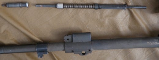M27 gas system disassembled. Top left is the gas piston, this is the dirtiest part on the entire gun and is very simple to clean. Top right is gas piston rod which has a captive spring enclosed. The rod beyond the beveled half casing intrudes into the upper receiver and makes contact with the bolt carrier during operation. The Gas block is positioned just behind the bayonet stud and has a gas port facing downrange.