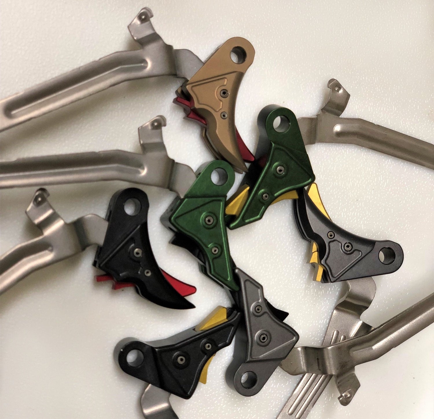 A variety of Overwatch Precision's previous TAC trigger offerings, in black, gunmetal gray, MIL green, and FDE flavors.